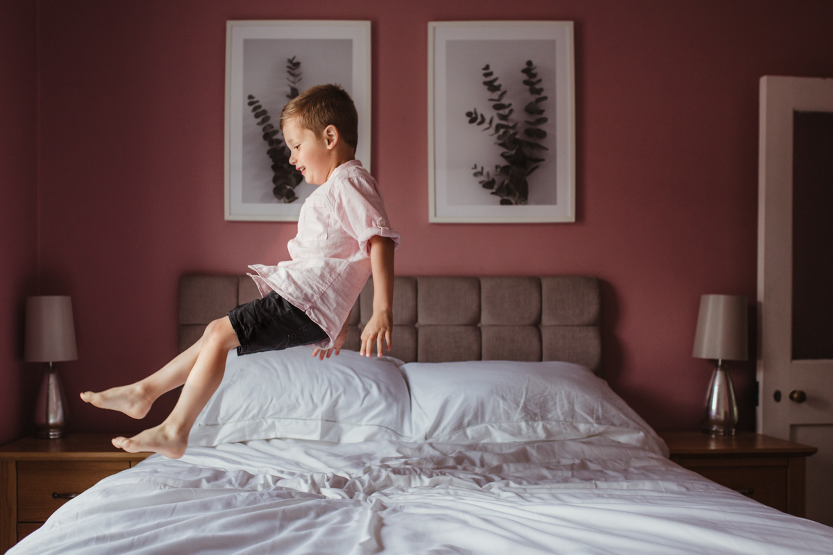 boy jumping on bed pink wall